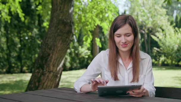 Young Lady Using an iPad in the Park - Materiał filmowy, wideo