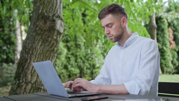Ένας νεαρός άνδρας, χρησιμοποιώντας ένα φορητό υπολογιστή στο πάρκο - Πλάνα, βίντεο