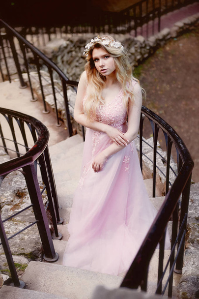 Portrait of a beautiful bride blond girl in pink lace dress ,hair decoration, handmade. Tenderness.Is long old stairs with stones, manual clutch - 写真・画像