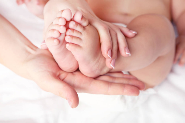 Newborn baby feets in mother hands on white bed - Photo, image