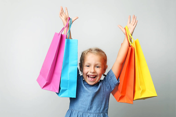Portrait of little girl holding shopping bags on grey background - Foto, afbeelding