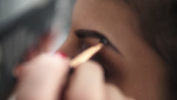 Closeup view of the makeup artists hands using brush to paint eyebrows for a model with false lashes. Slowmotion shot - Video