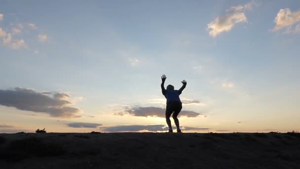 A fiatalember magasra ugrik, és taps a kezét, egy hegyvidéki területen, napnyugtakor a Slo-Mo - Felvétel, videó