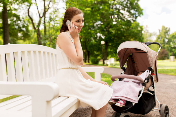 mother with stroller calling on smartphone at park - 写真・画像