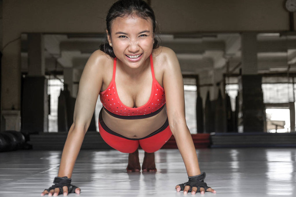 sexy suado ásia mulher no esporte roupas fazendo push ups no ginásio dojo chão sorrindo no duro treinamento fitness treino
 - Foto, Imagem