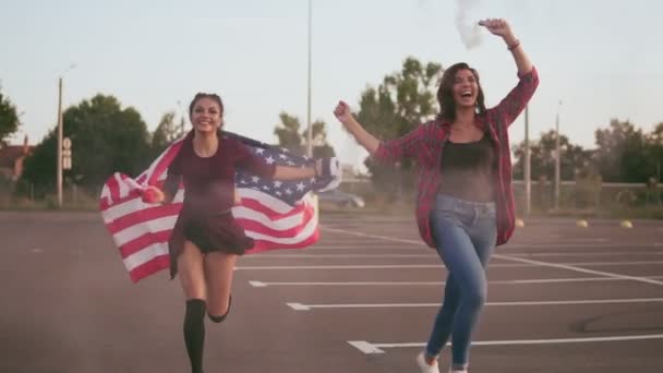 Mladí rádi americký bokovky dívky běží při držení americkou vlajku a vypustili granát kouřové bomby s bílou barvou, baví. Při pohledu na fotoaparát. Slowmotion shot - Záběry, video