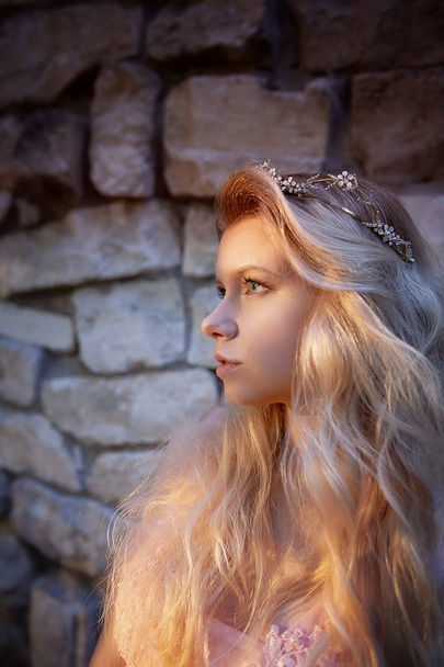 Portrait of a beautiful bride blond girl in pink lace dress ,hair decoration, handmade. Tenderness. Standing amid the old walls of stones, manual clutch.Hard interesting sunset color - Φωτογραφία, εικόνα