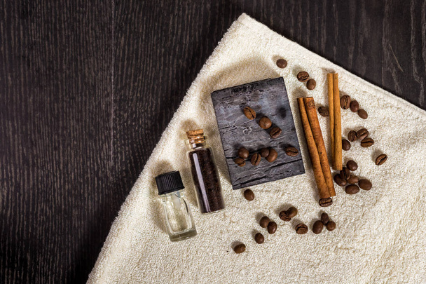 Set spa en marrón: jabón natural, aceite aromático, palitos de canela, granos de café y toalla sobre fondo de madera
. - Foto, Imagen