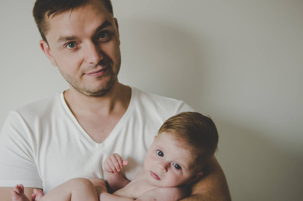 Young handsome father holding her little baby girl in hands and looking with tenderness on white background  - Fotografie, Obrázek