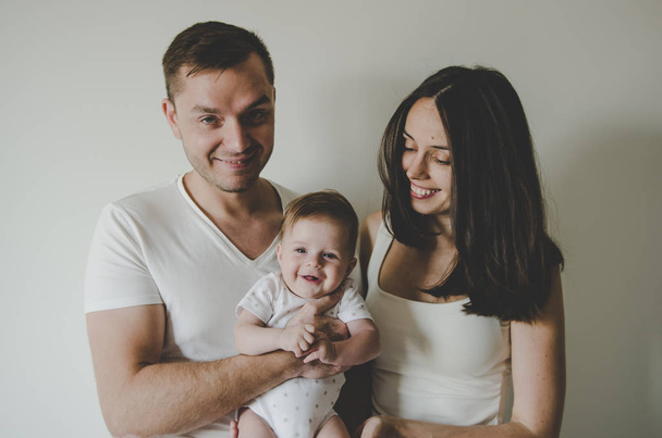 όμορφη νεαρή οικογένεια κρατώντας λίγο το μωρό χαμογελά σε λευκό φόντο  - Φωτογραφία, εικόνα