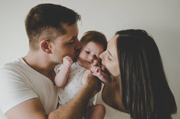 young parents holding little baby and kissing on white backgroun - Foto, Imagem