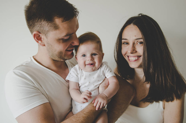 kaunis nuori perhe, jolla pieni vauva hymyilee valkoisella taustalla
  - Valokuva, kuva