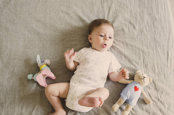 beautiful little baby lying on bed with her toys and looking on camera  - Foto, afbeelding