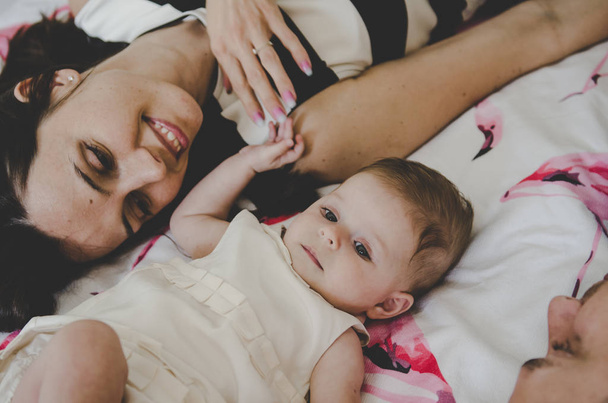 bela foto de jovem família com bebê menina deitada na cama e sorrindo
  - Foto, Imagem