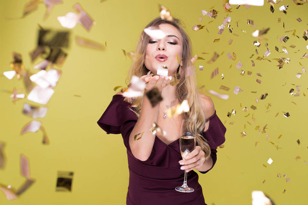 Beautiful young woman with champagne amuse and dancing. Girl blows off sequins. Happy New Year - Photo, Image