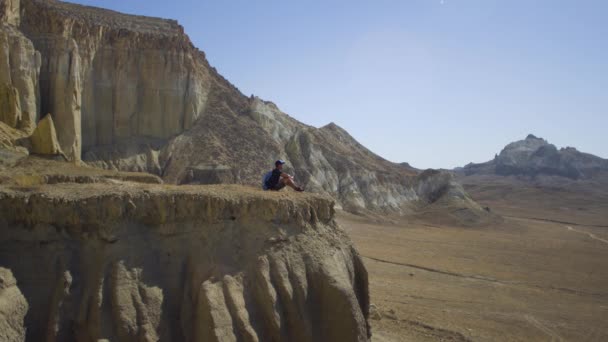 Młody podróżnik siedzi na skraju urwiska i pije wodę - Materiał filmowy, wideo