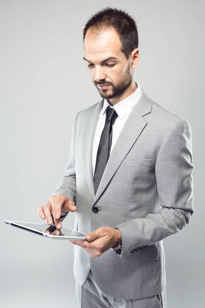 Geschäftsmann benutzt sein digitales Tablet vor grauem Hintergrund - Foto, Bild