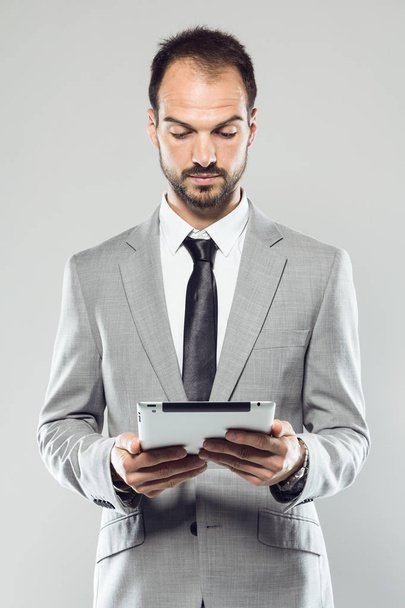 Business young man using his digital tablet over gray background - Photo, Image
