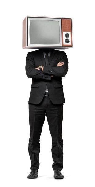 A businessman stands on white background with hands crossed and an old TV on his head. - Фото, изображение