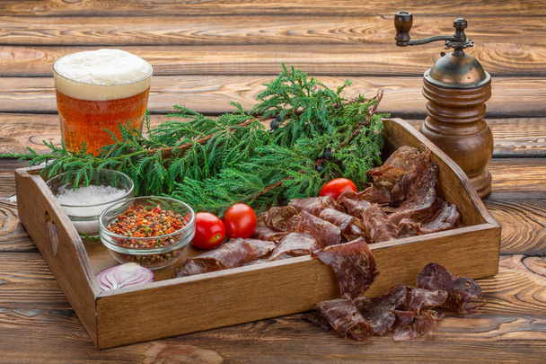 jerky beef with beer. Christmas still life of jerky with spices, large salt, cherry tomatoes and a tree branch on a wooden tray - Photo, Image