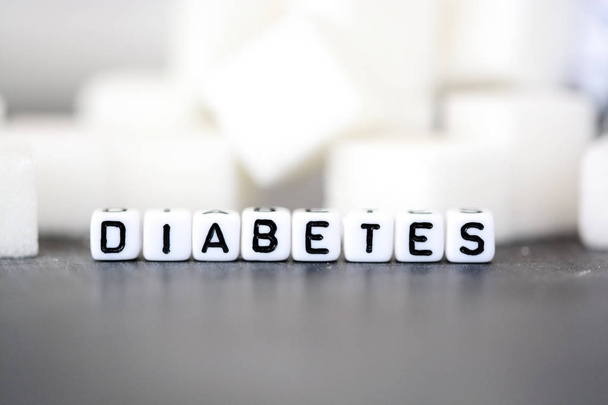 Diabetes-Krankheitskonzept mit weißen Buchstaben-Perlen vor einem Haufen Zuckerwürfel - Foto, Bild