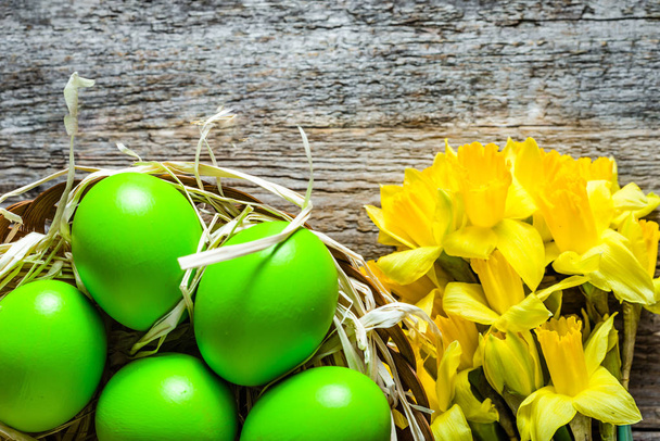 Background with easter eggs in the basket and daffodils on wood - Photo, image