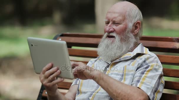 Atrakcyjny, starszy mężczyzna, za pomocą tabletu na ławce - Materiał filmowy, wideo