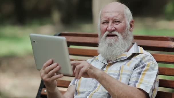 Atrakcyjny, starszy mężczyzna, za pomocą tabletu na ławce - Materiał filmowy, wideo
