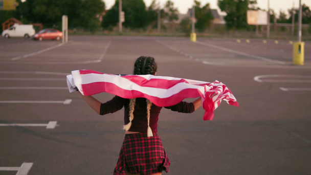 Rückansicht eines jungen, glücklichen amerikanischen Mädchens, das mit der amerikanischen Flagge läuft. Dann dreht sie sich um und blickt in die Kamera. Zeitlupenschuss - Filmmaterial, Video