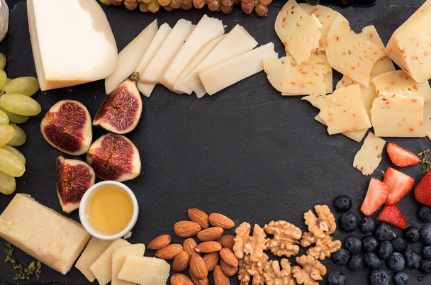 Tasting cheese dish with fruits, berries on old black cheeseboard. Food for wine and romantic, cheese delicatessen. Menu design horizontal. Top view. space for text - Foto, afbeelding