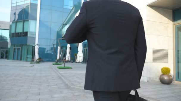 Following to young businessman with a briefcase walking near modern office building. Business man in sunglass commuting to work. Confident guy in suit going in the city. Slow motion Rear back view - Footage, Video