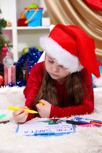 Beautiful little girl writes letter to Santa Claus in festively decorated room - Fotografie, Obrázek