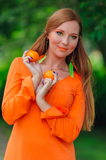 Portrait of pretty red hair woman with juicy delicious mandarins at summer green park. - Foto, Imagen