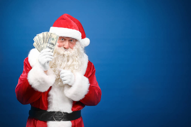 Santa Claus holding money on color background - Foto, afbeelding