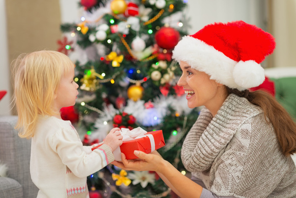 Baby girl presenting mother Christmas gift - Foto, afbeelding