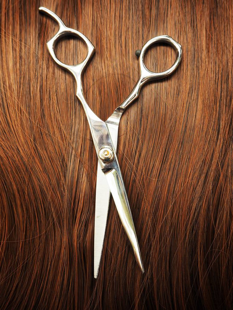 Metal hair cutting shears on brown hair - Foto, imagen