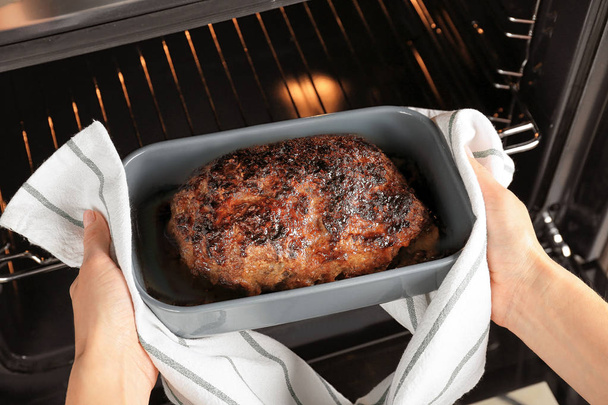 Woman taking out baked turkey meatloaf from oven, closeup - Foto, Bild