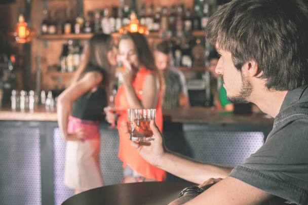 Drunk man sitting at bar, drinking cocktail, looking at girls - Foto, Imagen