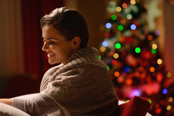 Happy young woman sitting chair in front of Christmas tree - Foto, Imagen