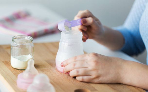 hands with bottle and scoop making formula milk - Foto, Imagen