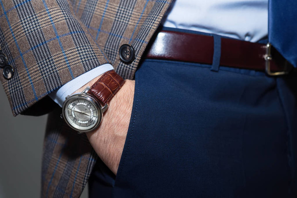 Closeup fashion image of luxury watch on wrist of man.body detail of a business man.Man's hand in checkered jacket,in dark blue pants pocket closeup.Casual outfit. Tonal in a business suit close up - Photo, image