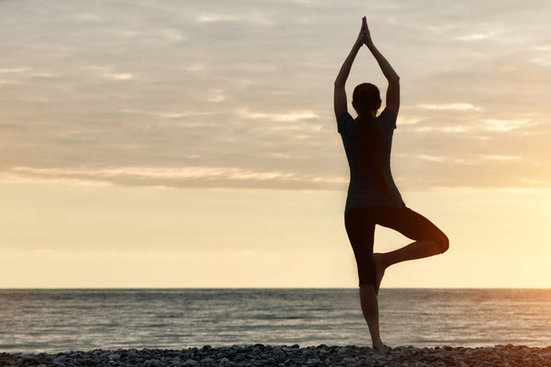 Meisje op zonsondergang praktizerende yoga bij de kust, achteraanzicht - Foto, afbeelding