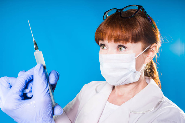 a girl in medical clothes, a mask and gloves is going to do an injection on a blue background, isolated - Photo, Image