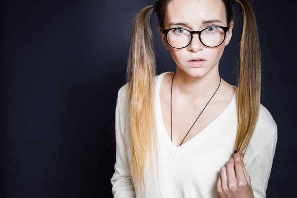a strict and frightened  girl with two tails and wearing glasses on a black background - Foto, Imagem