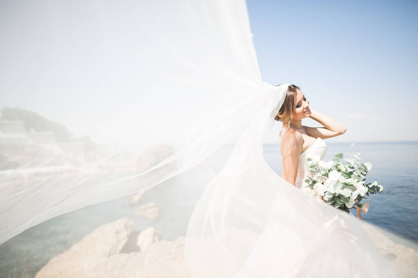 schöne Braut im weißen Brautkleid posiert in der Nähe des Meeres mit schönem Hintergrund - Foto, Bild