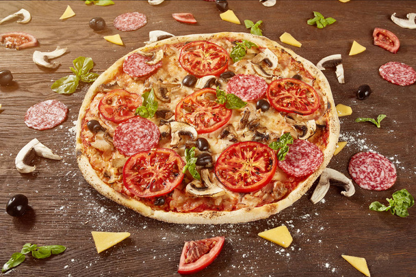 Pizza with tomatoes, mozzarella cheese, black olives and basil. Delicious italian pizza on wooden pizza board. - 写真・画像
