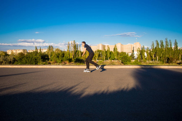 Щасливий молодий чоловік катається на роликах у міському парку на заході сонця
 - Фото, зображення