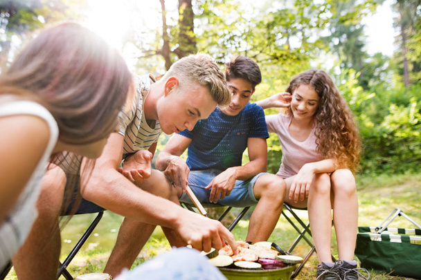 Teenagers camping, cooking vegetables on barbecue grill. - 写真・画像