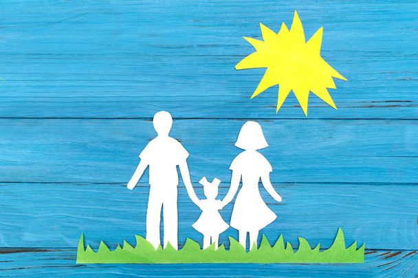 Silhouette en papier d'une famille debout sur l'herbe verte sous le soleil sur fond de bois bleu. Concept d'amour familial
 - Photo, image