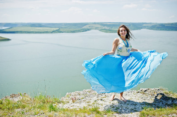 Brunette girl, wear on blue dress stands barefoot at cliff with  - Фото, зображення